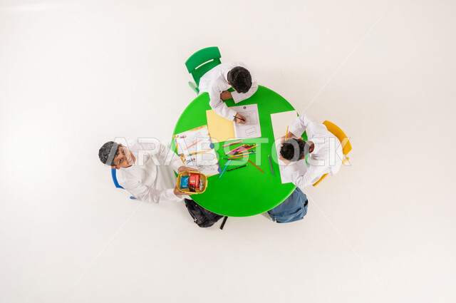 تعلم مهارات التركيز والابتكار للطلاب في مدارس المملكة العربية السعودية، تلاميذ يقومون بنشاطات ابداعية ترفيهية، بورتريه علوي عامودي لولد عربي خليجي سعودي يرتدي الثوب التقليدي يقوم بتناول وجبة خفيفة في  وقت الاستراحة، خلفية بيضاء