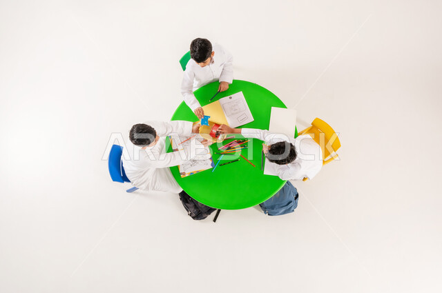 أنشطة ترفيهية مسلية، تبادل الوجبات الخفيفة في وقت الاستراحة، تعلم مهارات التركيز والابتكار، مفهوم الاهتمام بالهوايات، تعزيز المواهب الابداعية عند الطلاب، بورتريه علوي عامودي لتلاميذ عرب خليجيين سعوديين يرتدون الزي التقليدي يقومون بالرسم والتلوين، خلفية بيضاء