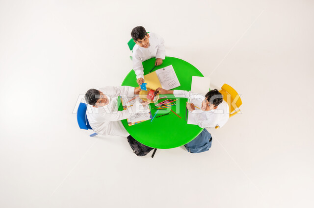 تبادل الوجبات الخفيفة في وقت الاستراحة، تعلم مهارات التركيز والابتكار، مفهوم الاهتمام بالهوايات، تعزيز المواهب الابداعية عند الطلاب، أنشطة ترفيهية مسلية، بورتريه علوي عامودي لتلاميذ عرب خليجيين سعوديين يرتدون الزي التقليدي يقومون بالرسم والتلوين، خلفية بيضاء