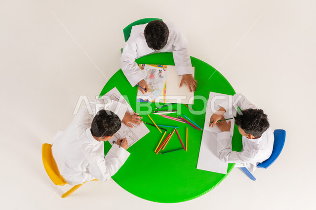 تعلم مهارات التركيز والابتكار، مفهوم الاهتمام بالهوايات، تعزيز المواهب الابداعية عند الطلاب، أنشطة ترفيهية مسلية، بورتريه علوي عامودي لتلاميذ عرب خليجيين سعوديين يرتدون الزي التقليدي يقومون بالرسم والتلوين، خلفية بيضاء