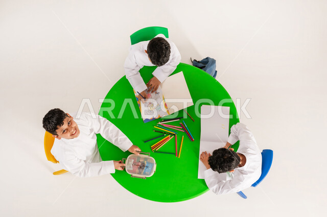 تلاميذ يقومون بنشاطات ابداعية ترفيهية، تعلم مهارات التركيز والابتكار للطلاب في مدارس المملكة العربية السعودية، بورتريه علوي عامودي لولدعربي خليجي سعودي يرتدي الثوب التقليدي يقوم بتناول وجبة خفيفة في  وقت الاستراحة، خلفية بيضاء