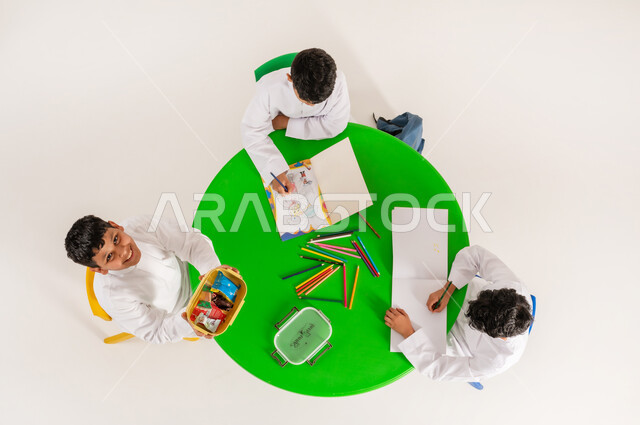 Learning concentration and innovation skills for students in Saudi Arabia schools, students doing creative and entertaining activities, vertical top portrait of a Saudi Arabian Gulf boy wearing traditional dress having a snack during break time, white background