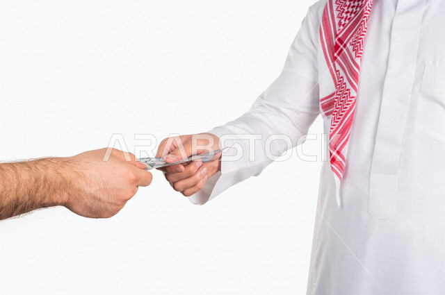 Portrait of a Saudi Arabian Gulf man receiving a sum of money from the hand of another person, paper currency for the Saudi riyal, the concept of business financing, saving and saving money, paper money