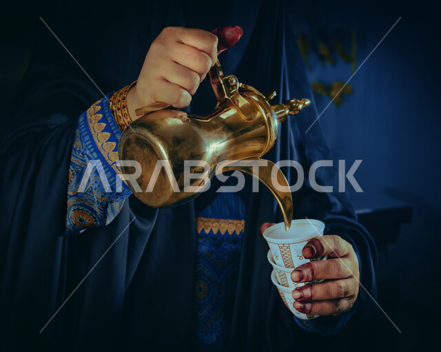 ذكرى تأسيس الدولة السعودية الاولى 22 فبراير، مفهوم الكرم وحسن الاستقبال، يوم بدينا 1727 م، الاحتفال بالمناسبات والأعياد الوطنية، صورة مقربة لأيدي شابة عربية خليجية سعودية ترتدي الأزياء التراثية تقوم بصب القهوة من الدلة النحاسية
