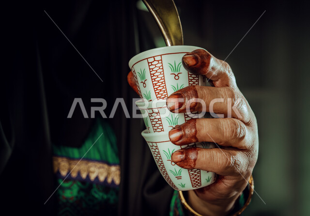 ذكرى تأسيس الدولة السعودية الاولى 22 فبراير، مفهوم الكرم وحسن الاستقبال، يوم بدينا 1727 م، الاحتفال بالمناسبات والأعياد الوطنية، صورة مقربة لأيدي شابة عربية خليجية سعودية ترتدي الأزياء التراثية تقوم بصب القهوة من الدلة النحاسية