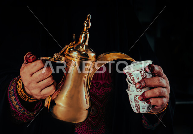 ذكرى تأسيس الدولة السعودية الاولى 22 فبراير، مفهوم الكرم وحسن الاستقبال، يوم بدينا 1727 م، الاحتفال بالمناسبات والأعياد الوطنية، صورة مقربة لأيدي شابة عربية خليجية سعودية ترتدي الأزياء التراثية تقوم بصب القهوة من الدلة النحاسية