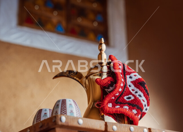 تقديم المنتجات المحلية للضيوف، مفهوم الكرم وحسن الاستقبال، ذكرى تأسيس الدولة السعودية الاولى 22 فبراير، يوم بدينا 1727 م، الاحتفال بالمناسبات والأعياد الوطنية، صورة مقربة لدلة قهوة نحاسية مع فناجين على طاولة خشبية