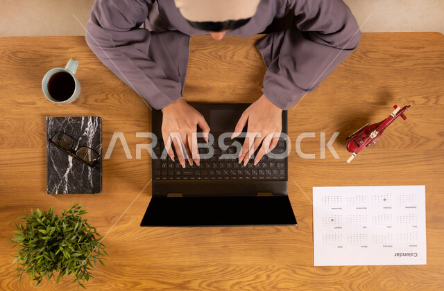 الحصول على المستلزمات اللازمة عن طريق الاونلاين، الاستعداد لقضاء رحلة صيفية ممتعة، مفهوم السياحة والقيام بالجولات الترفيهية، صورة علوية عامودية لإمرأة عربية خليجية سعودية تستخدم جهاز الحاسوب المحمول، دمج التكنولوجيا في الحياة العملية