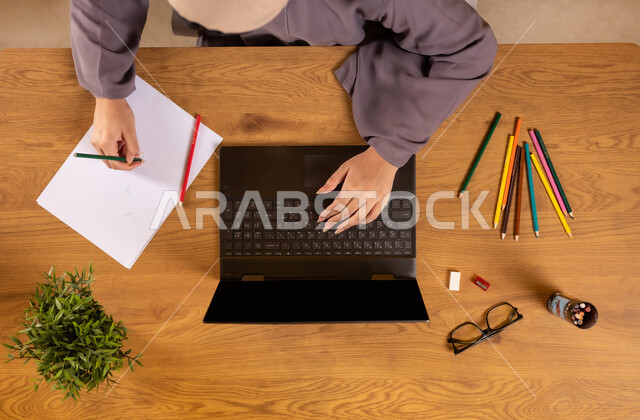 الاهتمام بالنشاطات والهوايات، التعلم والتدريب من خلال المواقع الالكترونية، ممارسة موهبة الرسم والتلوين، صورة علوية عامودية لإمرأة عربية خليجية سعودية تستخدم الحاسوب المحمول وتقوم برسم تصاميم فنية مميزة، الاستمتاع بالفنون اليدوية، استخدام التكنولوجيا الحديثة