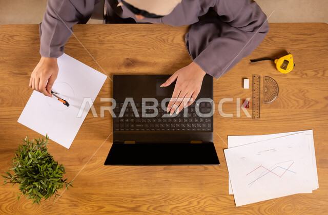 دمج التكنولوجيا في الحياة العلمية، استخدام التقنيات الحديثة والمتطورة، تعلم الحساب والرياضيات من خلال المواقع الالكترونية، صورة علوية عامودية لإمرأة عربية خليجية سعودية تستخدم جهاز الحاسوب تقوم برسم المخططات البيانية