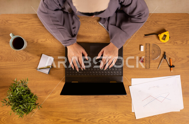 Learning arithmetic and mathematics through websites, arithmetic training through online programs, integrating technology into scientific life, using modern and advanced technologies, vertical top view of a Saudi Arabian Gulf woman using a laptop, drawing graphs