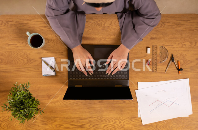 Learning arithmetic and mathematics through websites, arithmetic training through online programs, integrating technology into scientific life, using modern and advanced technologies, vertical top view of a Saudi Arabian Gulf woman using a laptop, drawing graphs