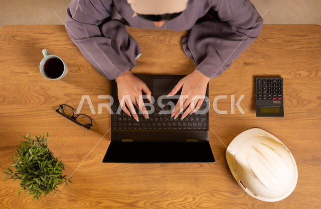 تدقيق المشاريع والخطط الهندسية، دمج التكنولوجيا والأجهزة الحديثة في الحياة العملية، استخدام الآلة الحاسبة لإجراء العمليات الحسابية، صورة علوية عامودية لإمرأة عربية خليجية سعودية تستخدم الحاسوب المحمول، مهن ووظائف نسائية مكتبية