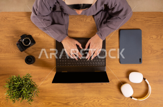 استخدام التقنيات الحديثة والمتطورة، صورة علوية عامودية لإمرأة عربية خليجية سعودية تقوم باستخدام جهاز الحاسوب المحمول، دمج التقنية و التكنولوجيا في العمل، التدريب من خلال الإنترنت، تعديل اللقطات والصور عبر تطبيقات وبرامج اللابتوب، التسوق عبر المواقع الالكترونية