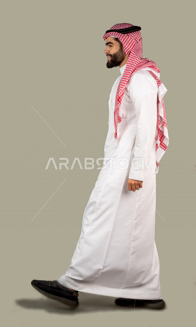 بورتريه جانبي لرجل عربي خليجي سعودي وسيم  يرتدي الزي السعودي التقليدي ، يمشي باتجاه جانبي ، ايماءات و تعابير للوجه و اليدين ، خلفية رمادية