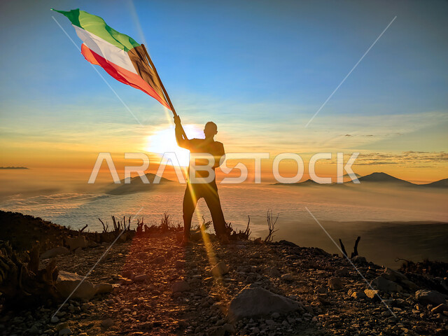 رفع علم الكويت عاليا، مناسبات وأعياد وطنية، الاحتفال بالعيد الوطني الكويتي 25 فبراير، صورة ظلية من الخلف لرجل يرفع الراية وقت غروب الشمس، إحياء ذكرى يوم العلم، حب الوطن والإنتماء اليه، الفخر والإعتزاز بالرموز والثقافة الكويتية