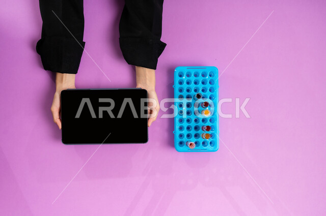 تدوين نتائج التحاليل المخبرية على التابليت، إجراء تجارب وبحوث علمية عبر التكنولوجيا الحيوية، البحث والتطوير العلمي في مجال الكيمياء، عرض شاشة سوداء فارغة، بورتريه علوي عامودي ليد إمرأة عربية سعودية خليجية تمسك جهاز الآيباد وبجانبها أنابيب الاختبار، خلفية وردية