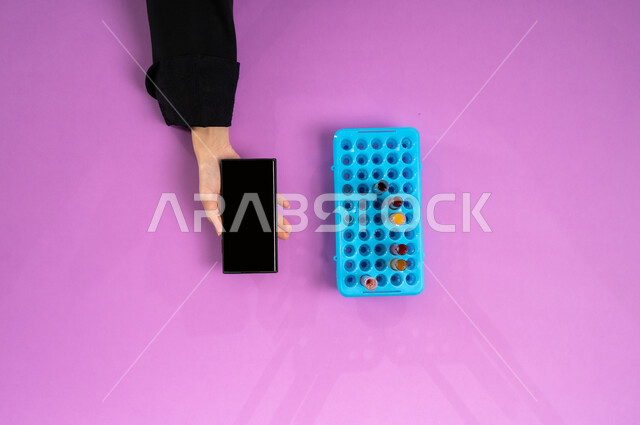 البحث والتطوير العلمي في مجال الكيمياء، عرض شاشة سوداء فارغة، بورتريه علوي عامودي ليد إمرأة عربية سعودية خليجية تمسك جهاز الجوال وبجانبها أنابيب الاختبار، تدوين نتائج التحاليل المخبرية على الموبايل، خإجراء تجارب وبحوث علمية عبر التكنولوجيا الحيوية، لفية وردية