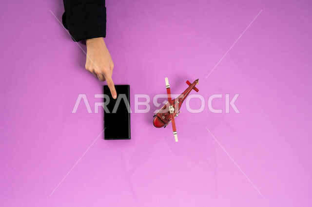 الاستعداد لقضاء رحلة صيفية ممتعة، عرض شاشة سوداء فارغة، بورتريه علوي عامودي ليد إمرأة عربية خليجية سعودية تستخدم الجوال وبجانبها مجسم طائرة، قطع تذاكر الطيران أونلاين، استخدام الانترنت للبحث عن رحلات جوية، مفهوم السياحة والقيام بالجولات الترفيهية، خلفية وردية