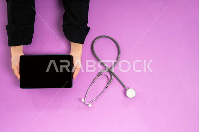 عرض شاشة سوداء فارغة، طلب استشارة صحية أونلاين، مفهوم الطب والرعاية الصحية، الخدمات والأجهزة الطبية، التسويق للأدوات الحديثة، بورتريه علوي عامودي ليدين إمرأة عربية سعودية خليجية تقوم بإجراء البحوث والدراسات عبر جهاز التابلت وبجانبها السماعة الطبية، خلفية وردية