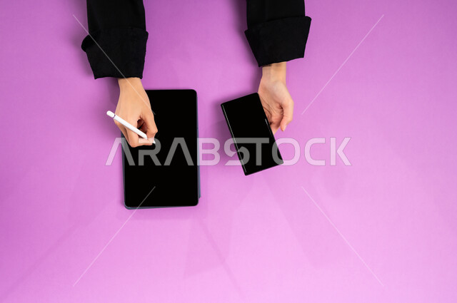 إنجاز المهام المطلوبة عن بعد، بورتريه علوي عامودي ليدين إمرأة عربية خليجية سعودية تعمل على التابليت والجوال، عرض شاشة سوداء فارغة، مهن ووظائف مكتبية سعودية، دمج العمل مع التقنية والتكنولوجيا الحديثة، مفهوم ادارة الاعمال وتحقيق الأهداف أونلاين، خلفية وردية