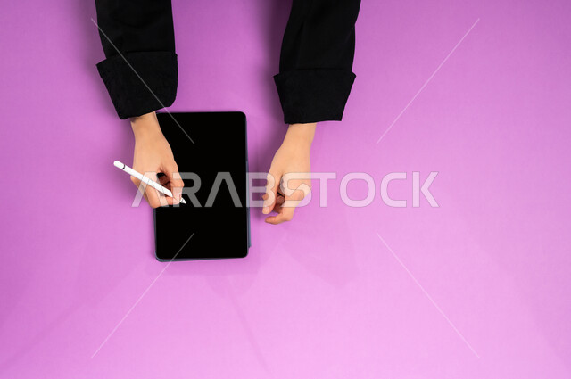 إنجاز المهام المطلوبة عن بعد، بورتريه علوي عامودي ليدين إمرأة عربية خليجية سعودية تعمل على جهاز التابليت، استخدام التقنيات الحديثة والمتطورة بالعمل، البيع والشراء عبر الانترنت، الاستفادة من تطبيقات التسوق أونلاين، عرض شاشة سوداء فارغة، خلفية وردية