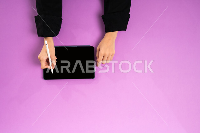 عرض شاشة سوداء فارغة، إنجاز المهام المطلوبة عن بعد، بورتريه علوي عامودي ليدين إمرأة عربية خليجية سعودية تعمل على جهاز التابليت، استخدام التقنيات الحديثة والمتطورة بالعمل، البيع والشراء عبر الانترنت، الاستفادة من تطبيقات التسوق أونلاين، خلفية وردية