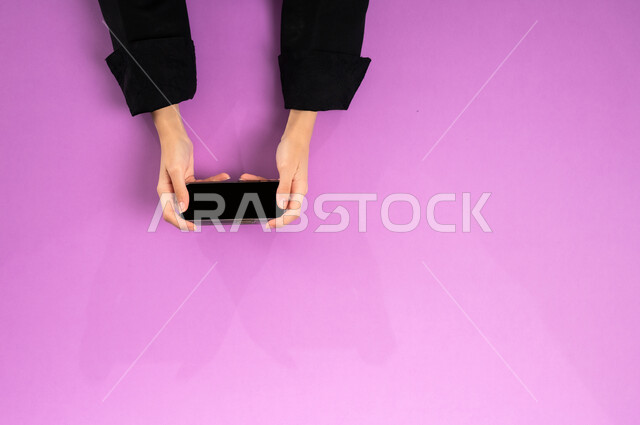 الاستفادة من تطبيقات التسوق أونلاين، عرض شاشة سوداء فارغة، إنجاز المهام المطلوبة عن بعد، بورتريه علوي عامودي ليدين إمرأة عربية خليجية سعودية تعمل على جهاز الهاتف المحمول، استخدام التقنيات الحديثة والمتطورة بالعمل، البيع والشراء عبر الانترنت، خلفية وردية