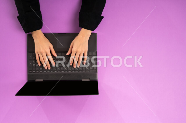 إنجاز المهام المطلوبة عن بعد، بورتريه علوي عامودي ليدين إمرأة عربية خليجية سعودية تعمل على جهاز الحاسب المحمول، عرض شاشة سوداء فارغة، مهن ووظائف مكتبية سعودية، دمج العمل مع التقنية والتكنولوجيا الحديثة، مفهوم ادارة الاعمال وتحقيق الأهداف أونلاين، خلفية وردية