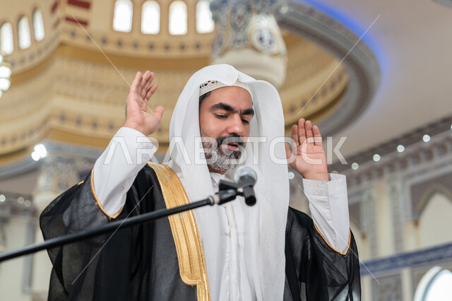 الشعور بالخشوع والطمأنينة, الركن الثاني من أركان الإسلام, أداء فرائض الدين الإسلامي, إمامة المسلمين في المسجد, إقامة الصلاة على وقتها، صورة مقربة لإمام عربي خليجي إماراتي يرتدي البشت والكندورة والغترة البيضاء يقوم بأداء فريضة الصلاة ويرفع يديه لتكبيرة الإحرام