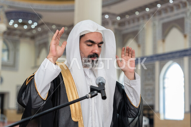 الركن الثاني من أركان الإسلام, الشعور بالخشوع والطمأنينة, أداء فرائض الدين الإسلامي, إمامة المسلمين في المسجد, إقامة الصلاة على وقتها، صورة مقربة لإمام عربي خليجي إماراتي يرتدي البشت والكندورة والغترة البيضاء يقوم بأداء فريضة الصلاة ويرفع يديه لتكبيرة الإحرام