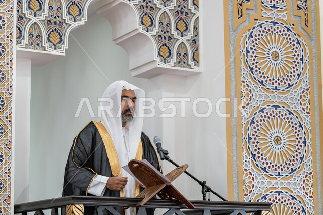 دور أئمة المساجد والخطباء في نشر الدين, توجيه الناس نحو الحق والهداية, تعزيز الروحانية الجماعية, مفهوم العبادة والتقرب إلى الله تعالى، إمام عربي خليجي إماراتي يرتدي البشت والكندورة والغترة البيضاء يقف على المنبر ويلقي خطبة يوم الجمعة
