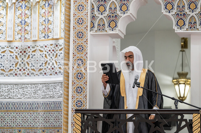 العبادة والتقرب إلى الله, الحث على أداء العبادات والفرائض الدينية, توجيه الناس لطريق الحق والهداية, إلقاء خطاب و دروس توجيهية على المسلمين, إمام مسجد عربي خليجي إماراتي يرتدي البشت والكندورة والغترة البيضاء يقف على المنبر ويلقي خطبة يوم الجمعة من الجهاز اللوحي