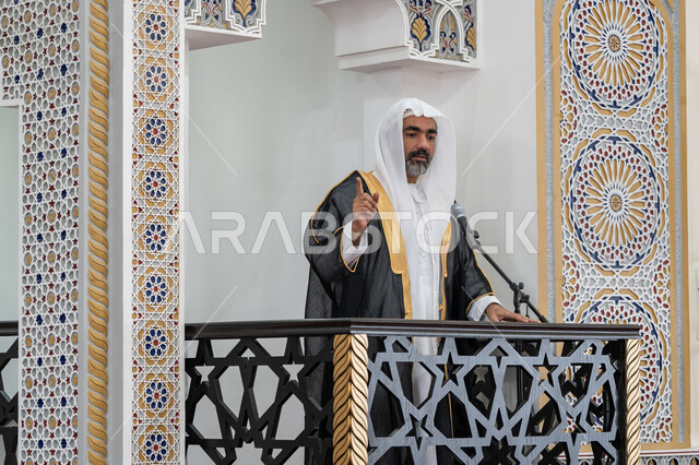 The concept of worship and drawing closer to God Almighty, guiding people towards truth and guidance, the role of mosque imams and preachers in spreading religion, an Arab Gulf Emirati imam wearing a bisht, kandura and white ghutra standing in front of the loudspeaker and delivering the sermon from the pulpit, a call to Muslims to perform the obligatory duties
