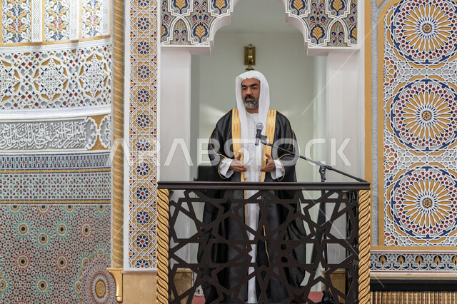 دور أئمة المساجد والخطباء في نشر الدين, مفهوم العبادة والتقرب إلى الله تعالى, توجيه الناس نحو الحق والهداية، إمام عربي خليجي إماراتي يرتدي البشت والكندورة والغترة البيضاء يقف أمام مكبر الصوت ويلقي الخطبة على المنبر, نداء المسلمين لأداء الفرائض