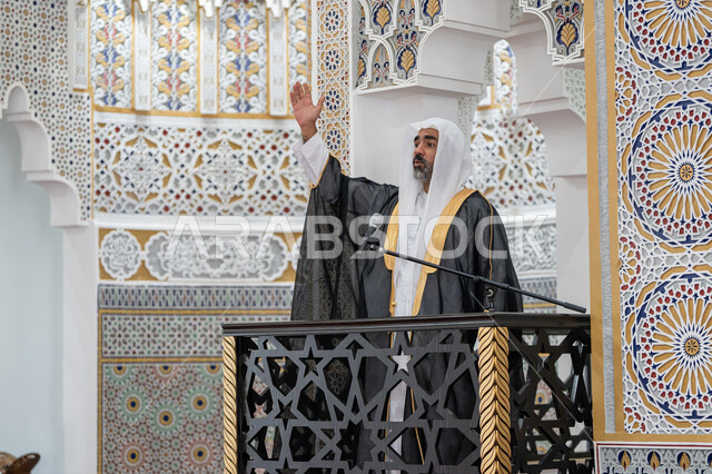 نداء المسلمين لأداء الفرائض, توجيه الناس نحو الحق والهداية, مفهوم العبادة والتقرب إلى الله تعالى, دور أئمة المساجد والخطباء في نشر الدين، إمام عربي خليجي إماراتي يرتدي البشت والكندورة والغترة البيضاء يقف أمام مكبر الصوت ويلقي الخطبة على المنبر