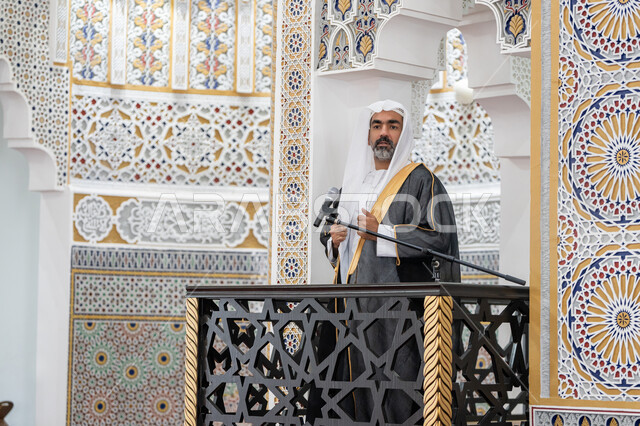 The concept of worship and drawing closer to God Almighty, guiding people towards truth and guidance, the role of mosque imams and preachers in spreading religion, an Arab Gulf Emirati imam wearing a bisht, kandura and white ghutra standing in front of the loudspeaker and delivering the sermon from the pulpit, a call to Muslims to perform the obligatory duties