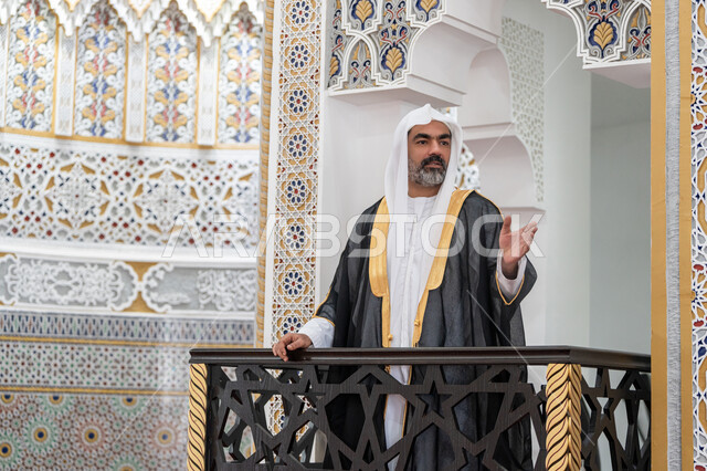 دور أئمة المساجد والخطباء في نشر الدين, مفهوم العبادة والتقرب إلى الله تعالى, توجيه الناس نحو الحق والهداية، إمام عربي خليجي إماراتي يرتدي البشت والكندورة والغترة البيضاء يقف أمام مكبر الصوت ويلقي الخطبة على المنبر, نداء المسلمين لأداء الفرائض