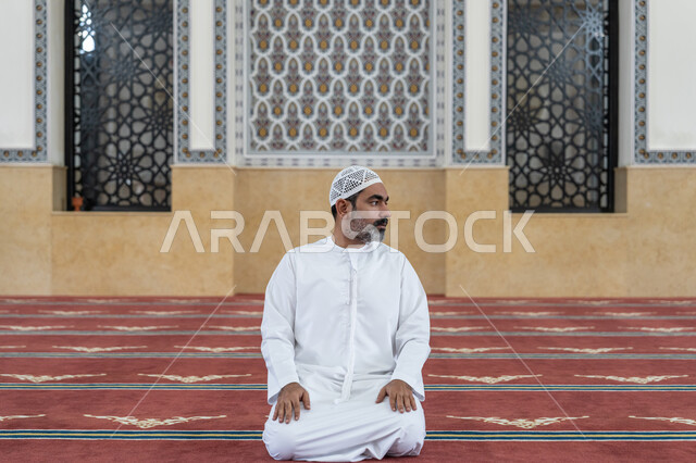 أداء الفرائض الدينية الإسلامية, إقامة الصلاة على وقتها, مفهوم أركان الإسلام، رجل عربي خليجي إماراتي يرتدي الكندورة والقبعة البيضاء يجلس في المسجد يقوم بالتسليم في ختام صلاته، الشعور بالخشوع والطمأنينة، العبادة والتقرب إلى الله