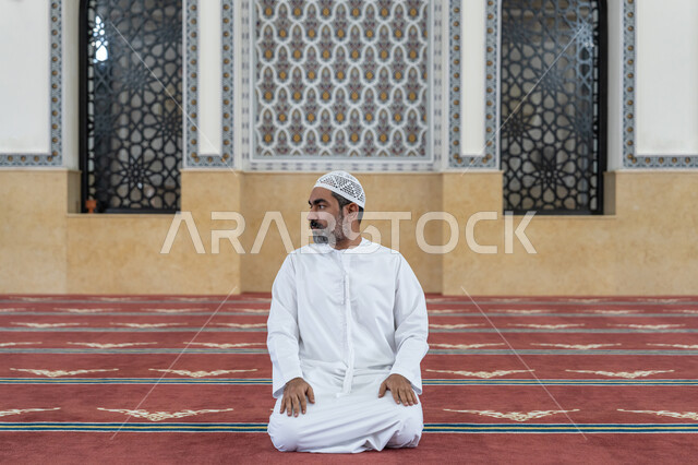 إقامة الصلاة على وقتها, مفهوم أركان الإسلام، أداء الفرائض الدينية الإسلامية، رجل عربي خليجي إماراتي يرتدي الكندورة والقبعة البيضاء يجلس في المسجد يقوم بالتسليم في ختام صلاته، الشعور بالخشوع والطمأنينة، العبادة والتقرب إلى الله