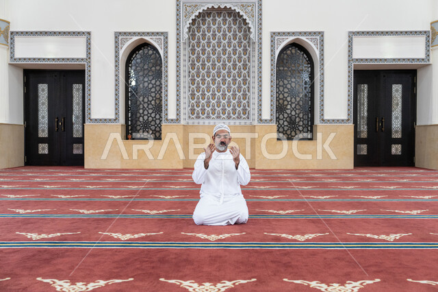 مفهوم الخشوع والتضرع, طلب الرحمة والمغفرة, العبادة والتقرب الى الله تعالى, رجل عربي خليجي اماراتي يرتدي الكندورة والقبعة البيضاء يجلس في إحدى المساجد ويرفع يديه للأعلى بتعابير الدعاء, أداء الفرائض الدينية الإسلامية، مفهوم أركان الإسلام