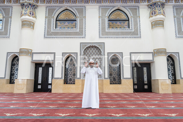 إقامة الصلاة على وقتها, العبادة والتقرب إلى الله، أداء الفرائض الدينية الإسلامية، الركن الثاني من أركان الإسلام، رجل عربي خليجي إماراتي يرتدي الكندورة والقبعة البيضاء يقف باستقامة يرفع يديه لتكبيرة الإحرام, الشعور بالخشوع والطمأنينة
