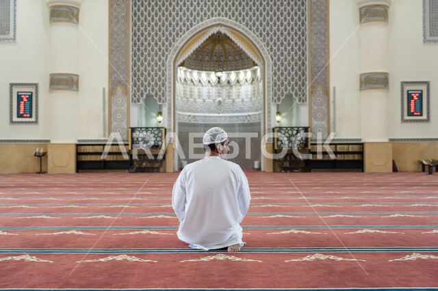 مفهوم أركان الإسلام, إقامة الصلاة على وقتها، أداء الفرائض الدينية الإسلامية، رجل عربي خليجي إماراتي يرتدي الكندورة والقبعة البيضاء يجلس في المسجد يقوم بالتسليم في ختام صلاته، الشعور بالخشوع والطمأنينة، العبادة والتقرب إلى الله