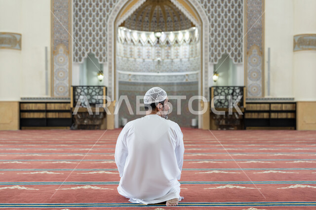 The concept of the pillars of Islam, performing prayers on time, performing Islamic religious duties, an Arab Gulf Emirati man wearing a kandura and a white hat sitting in the mosque, making the tasleem at the end of his prayer, feeling reverence and tranquility, worship and drawing closer to God
