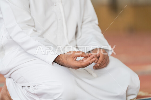 الاستغفار والدعاء وذكر الله, أذكار بعد الصلاة، مفهوم التعبد في بيوت الرحمن, أداء الفرائض الدينية الإسلامية, العبادة والتقرب الى الله, صورة مقربة لرجل عربي خليجي إماراتي يرتدي الكندورة يجلس في إحدى المساجد الإماراتية ويقوم بالتسبيح والتهليل