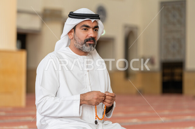 مفهوم التسبيح والتهليل, العبادة والتقرب الى الله تعالى, رجل عربي خليجي إماراتي يرتدي الكندورة والغترة البيضاء يجلس في إحدى المساجد ويمسك بيده سبحة، أداء الفرائض الدينية الإسلامية, أذكار بعد الصلاة، مفهوم التعبد في بيوت الرحمن