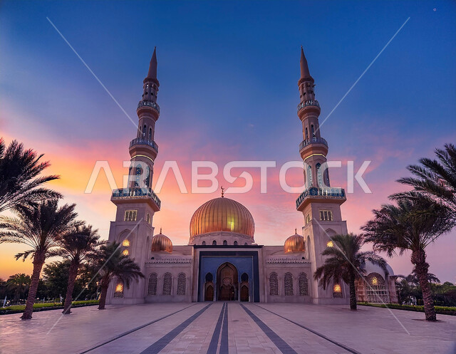 Call and invitation of Muslims to prayer, interest in planting palm trees in the mosque courtyard, view of a large mosque at sunset, concept of worship and closeness to God, architectural art of minarets and domes decorated in modern style, sacred religious places and landmarks in the Kingdom of Saudi Arabia