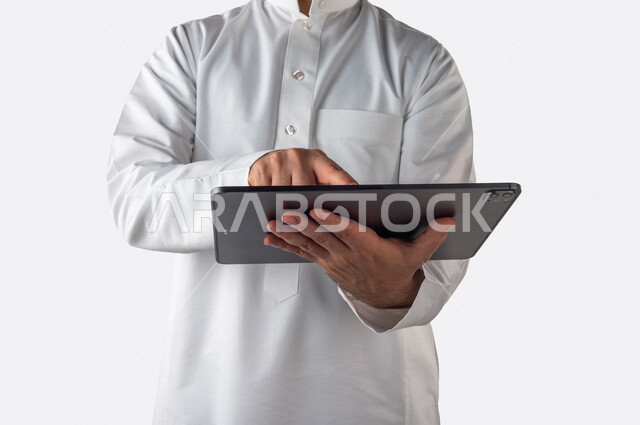 بورتريه لرجل خليجي سعودي يحمل بيده جهاز التابلت ، ينقر باصبعه على شاشة الجهاز التقني ، استخدام خاصية اللمس، استخدام اجهزة تقنية حديثة ، خلفية بيضاء