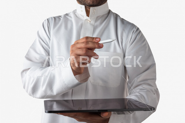 بورتريه لرجل خليجي سعودي يحمل بيده جهاز التابلت ، يستخدم القلم الخاص للضغط على شاشة الجهاز التقني ،تنظيم وادارة الاعمال عبر الجهاز التقني ، خلفية بيضاء