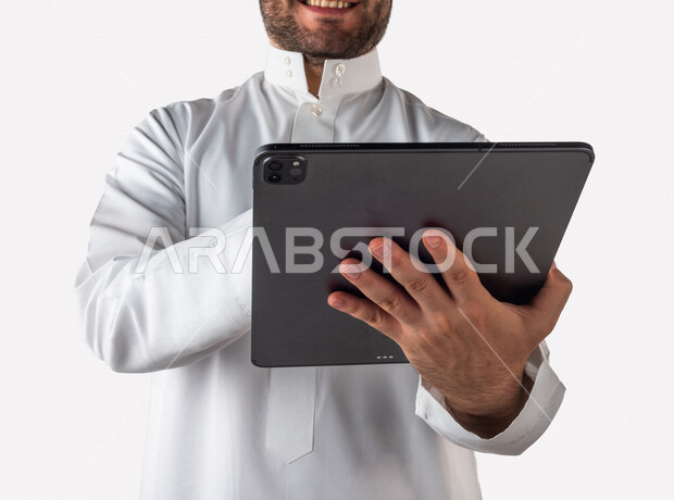 بورتريه لرجل خليجي سعودي يحمل بيده جهاز التابلت ، ينقر باصبعه على شاشة الجهاز التقني ، استخدام خاصية اللمس، استخدام اجهزة تقنية حديثة ، خلفية بيضاء